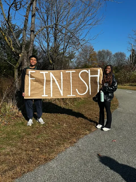 Two volunteers holding a handmade finish-line banner beside the race course.